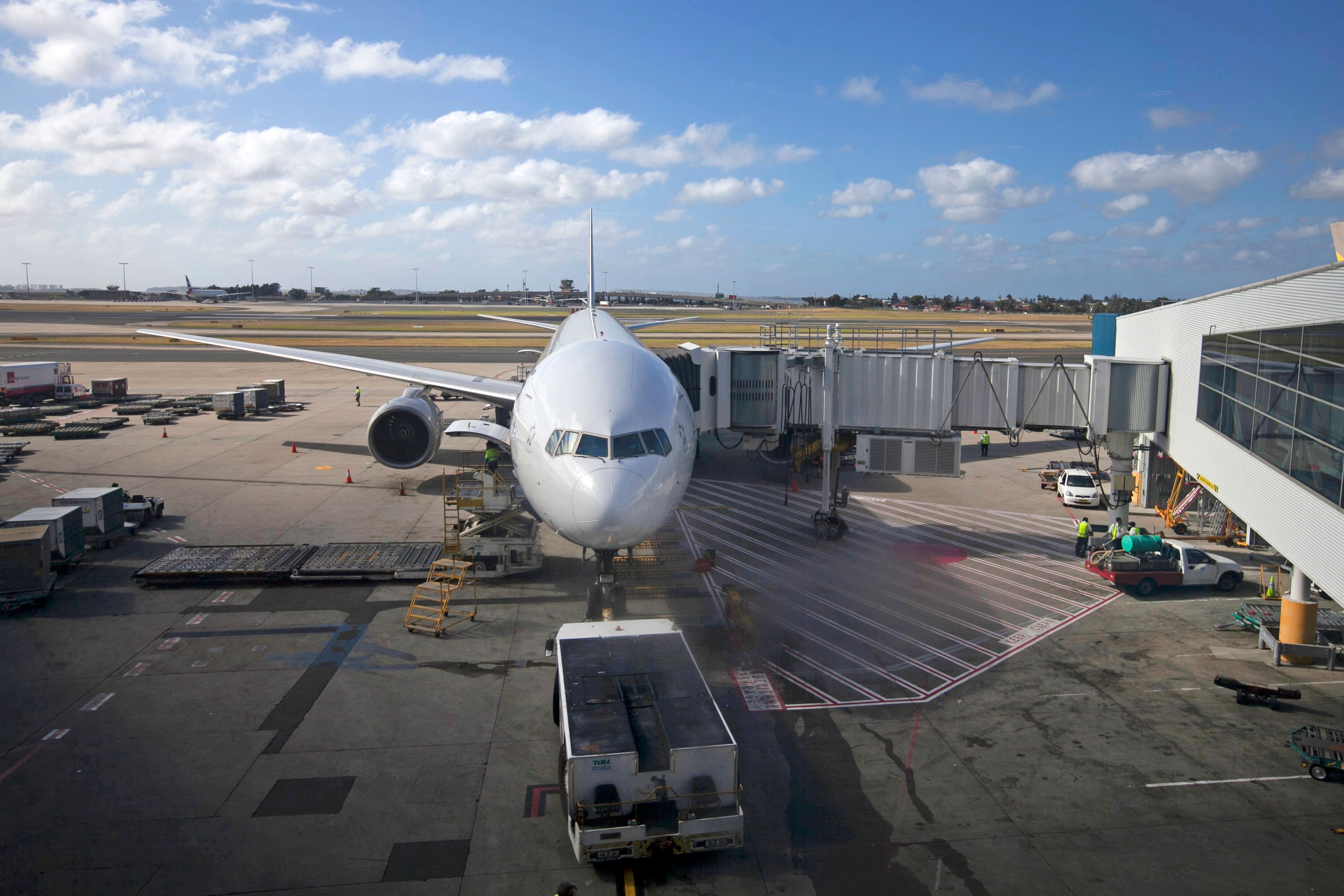 Commercial airliner connected to a jet bridge with ground-handling operations at an airport terminal